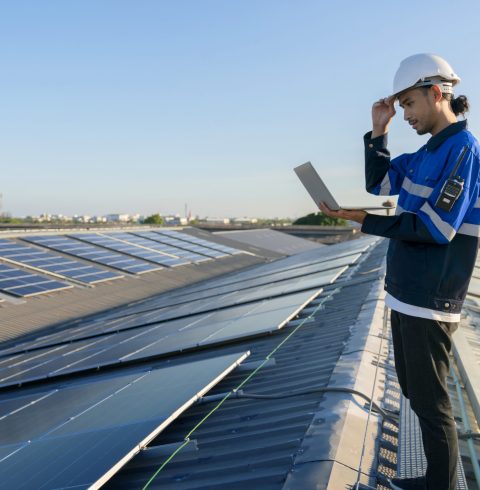 Specialist technician professional engineer with laptop and tablet maintenance checking installing solar roof panel on the factory rooftop under sunlight. Engineers holding tablet check solar roof.